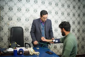 Profissional de saúde mede a pressão arterial de uma mulher durante consulta em ambiente clínico.