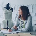 Designer planeja novas criações em um estúdio de moda, cercado por materiais e referências de trabalho.