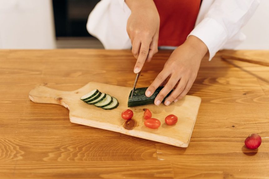 Mulher corta pepino e tomates-cereja para preparar uma salada em uma cozinha moderna.