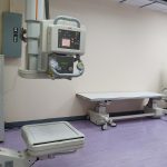Sala clínica com equipamentos de radiografia e mesa de exame em uma unidade de saúde