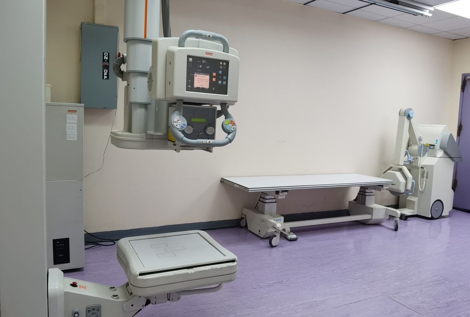 Sala clínica com equipamentos de radiografia e mesa de exame em uma unidade de saúde