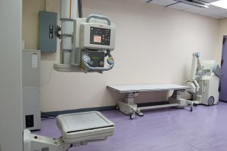 Sala clínica com equipamentos de radiografia e mesa de exame em uma unidade de saúde