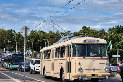 Trolebus circula por uma rua urbana arborizada, entre veículos e edifícios.