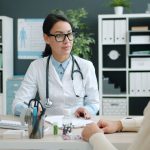 Médico conversa com uma paciente em uma clínica, discutindo opções de tratamento.